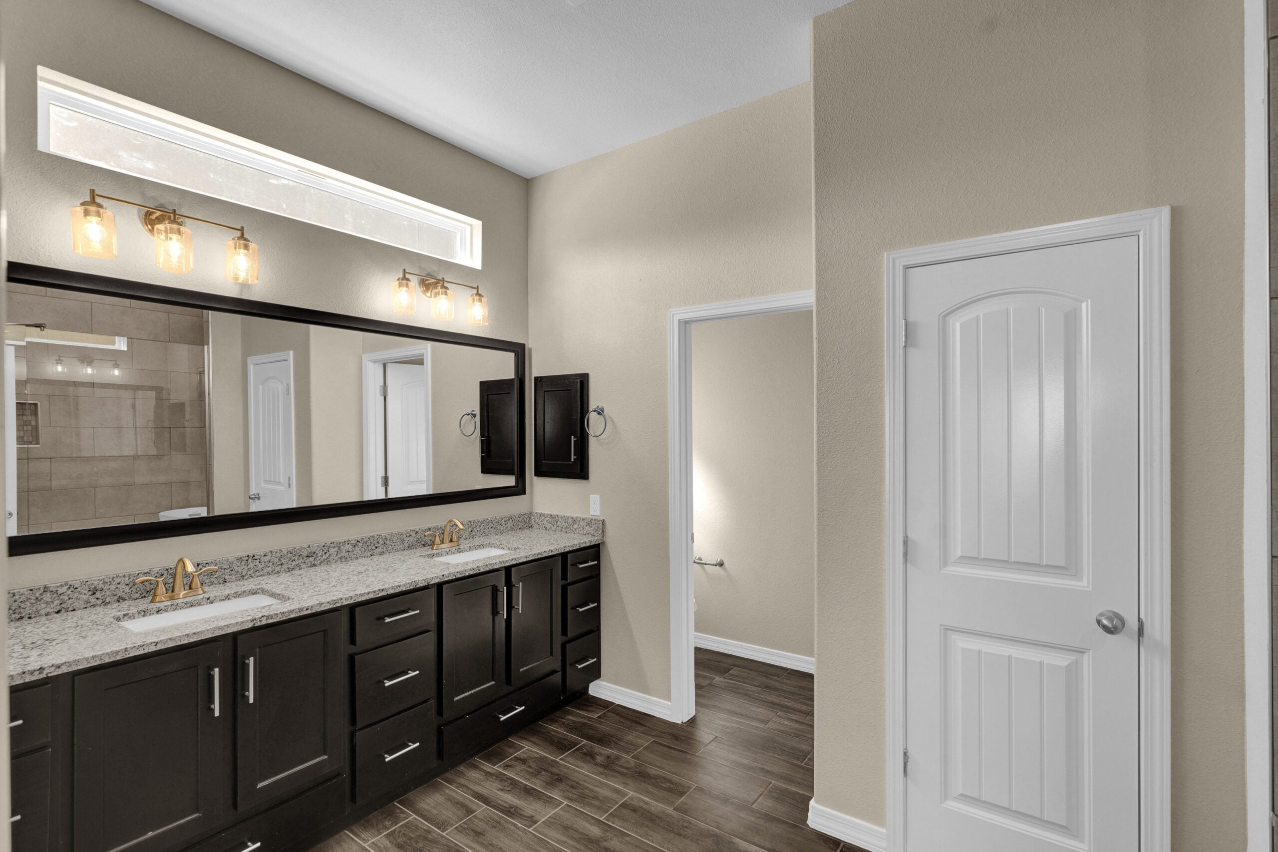 Primary bathroom in The Lavender model by Zia Homes, featuring a granite double vanity with dark wood cabinetry, large mirror, and modern glass pendant lighting.