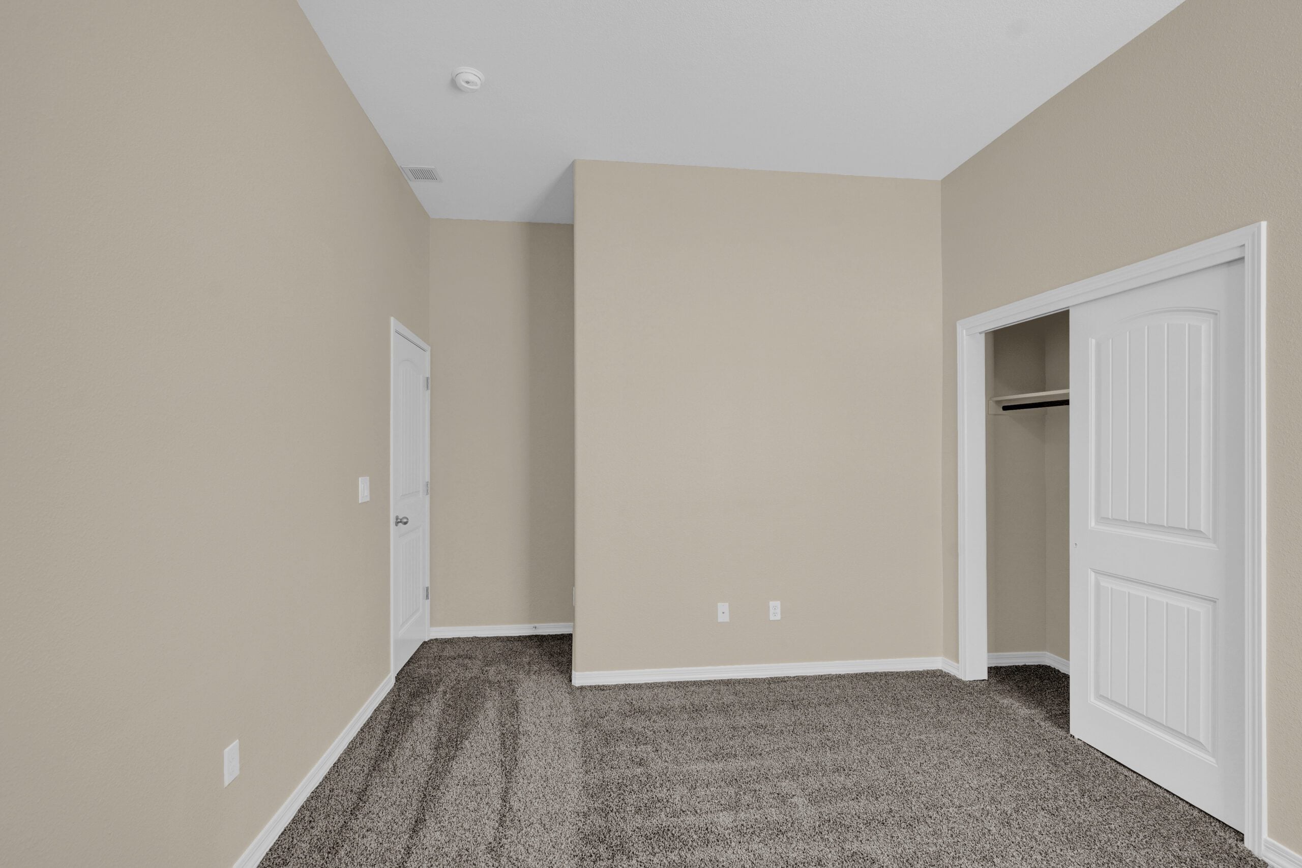 Secondary bedroom in The Lavender model by Zia Homes, featuring soft carpet flooring, neutral walls, and a built-in closet with white paneled sliding doors.