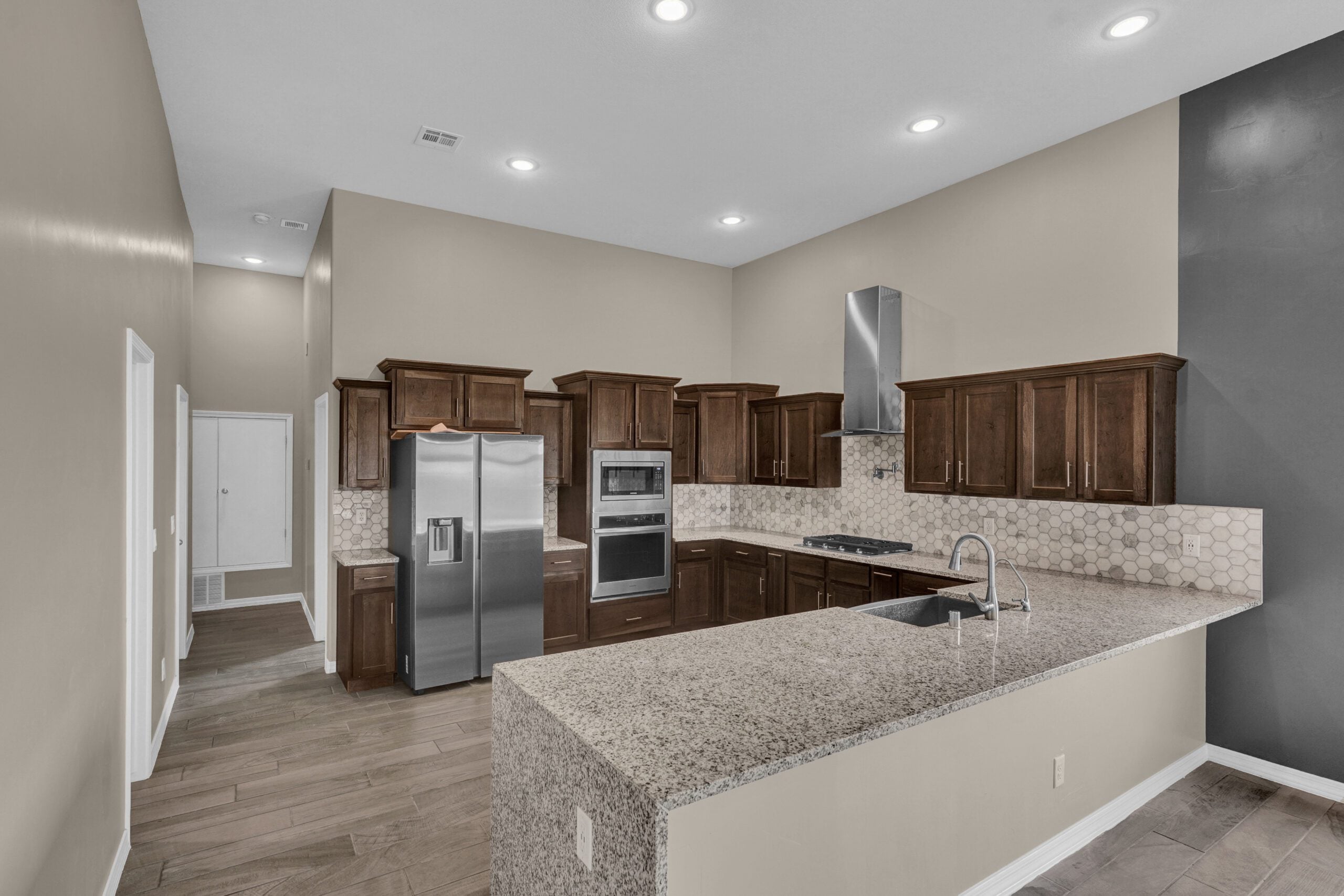 L-shaped kitchen in The Paprika model with granite island, wood cabinetry, and stainless steel appliances