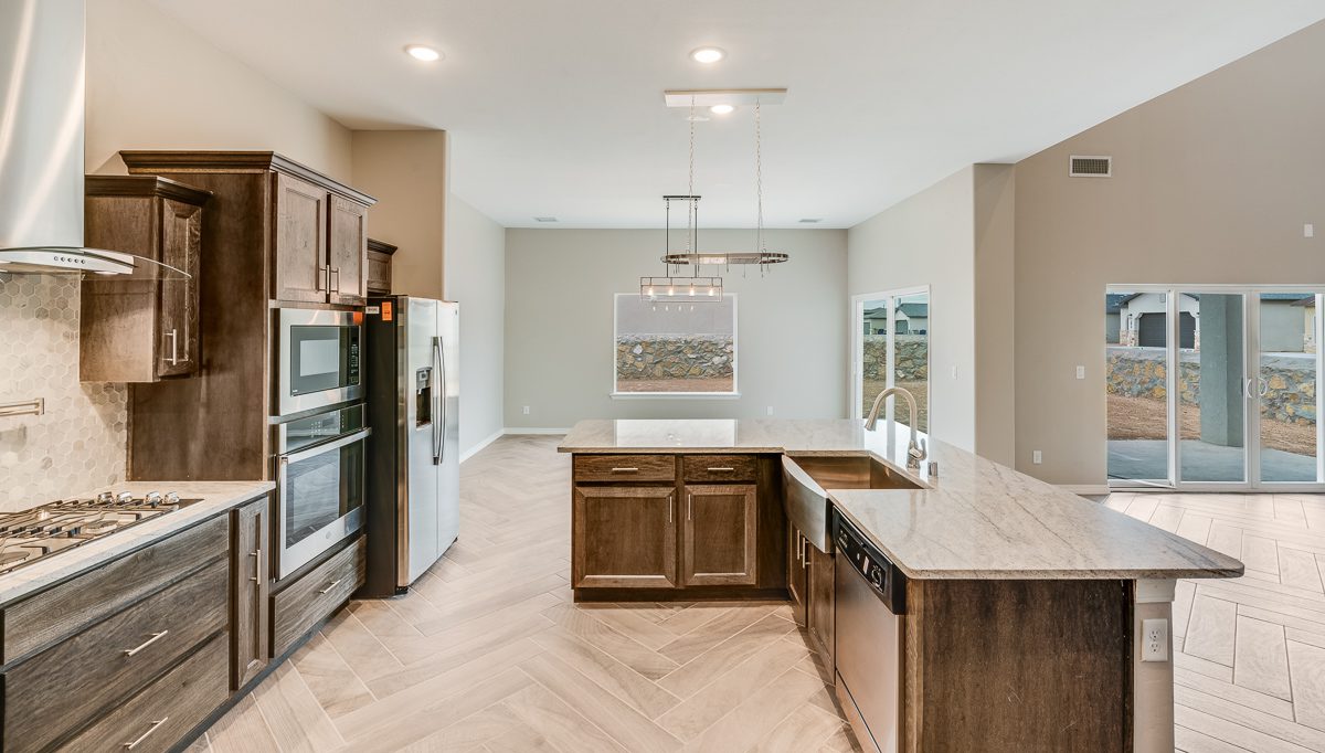 Alternate view of The Chiffon kitchen showcasing the central island with farmhouse sink, pendant lighting, built-in appliances, and backyard access through sliding glass doors.