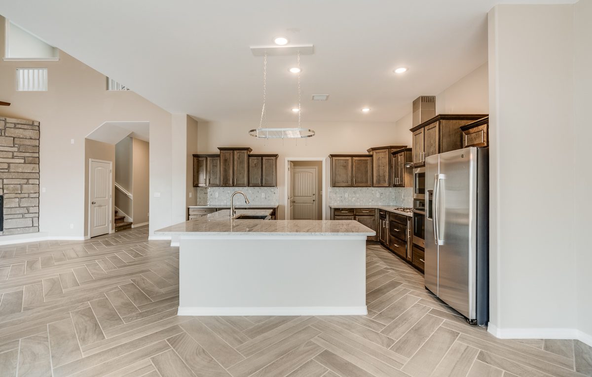 The Chiffon model kitchen with central island, stainless steel appliances, and dark wood cabinetry beneath pendant lighting.