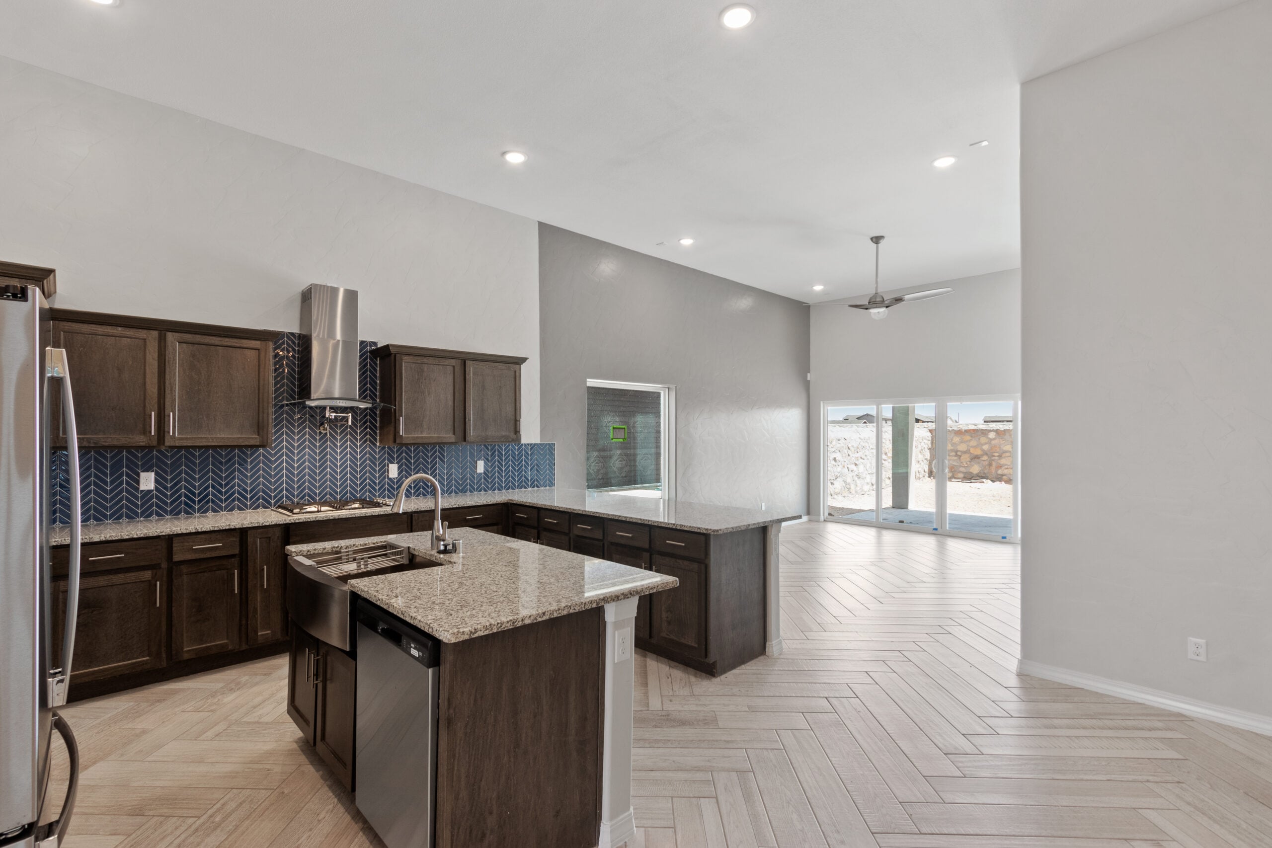 Modern kitchen in The Juniper home with dark wood cabinets, granite island, chevron backsplash, and view into dining and living area.