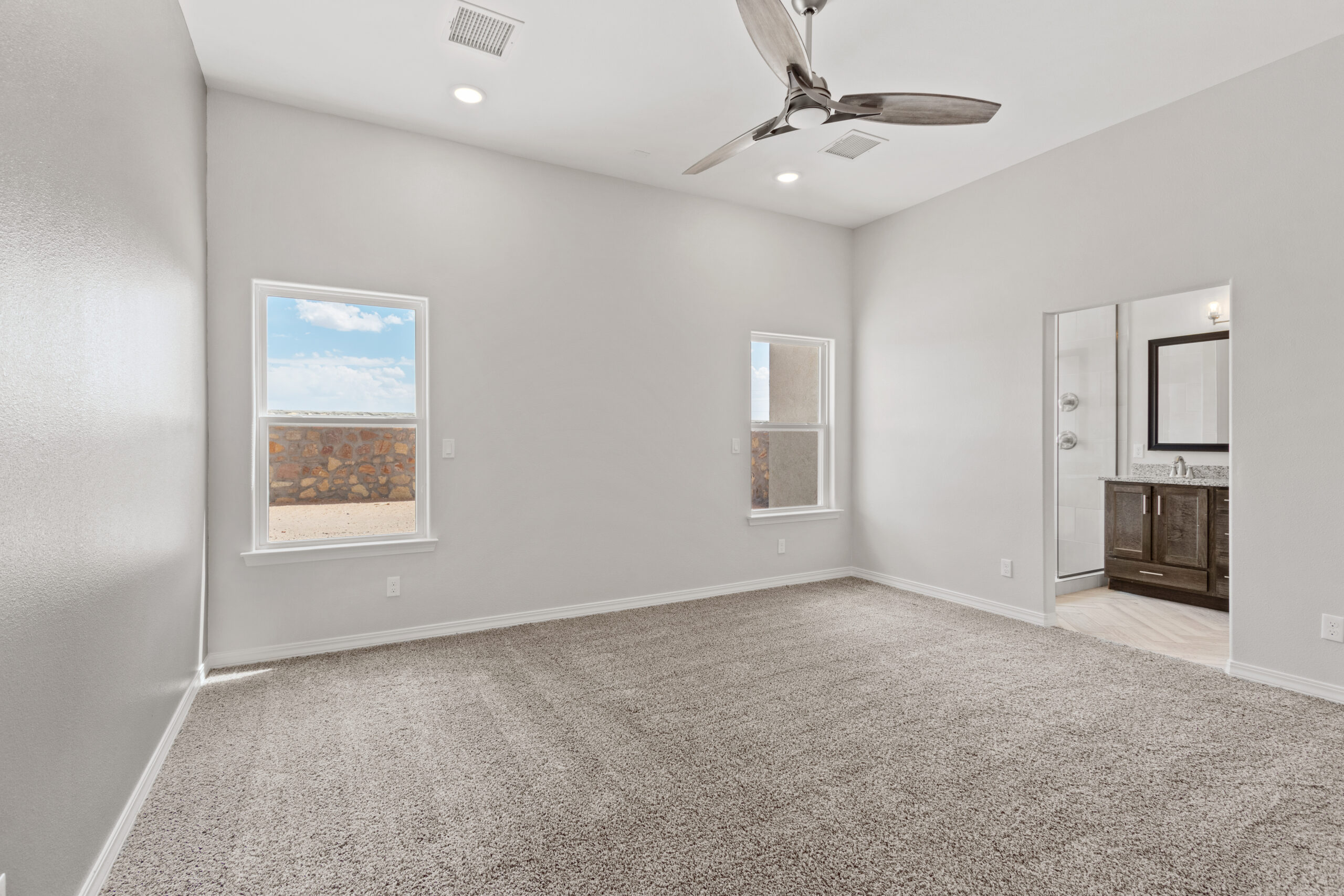 The Juniper’s primary bedroom with large windows, plush carpet, and direct access to a private bathroom.