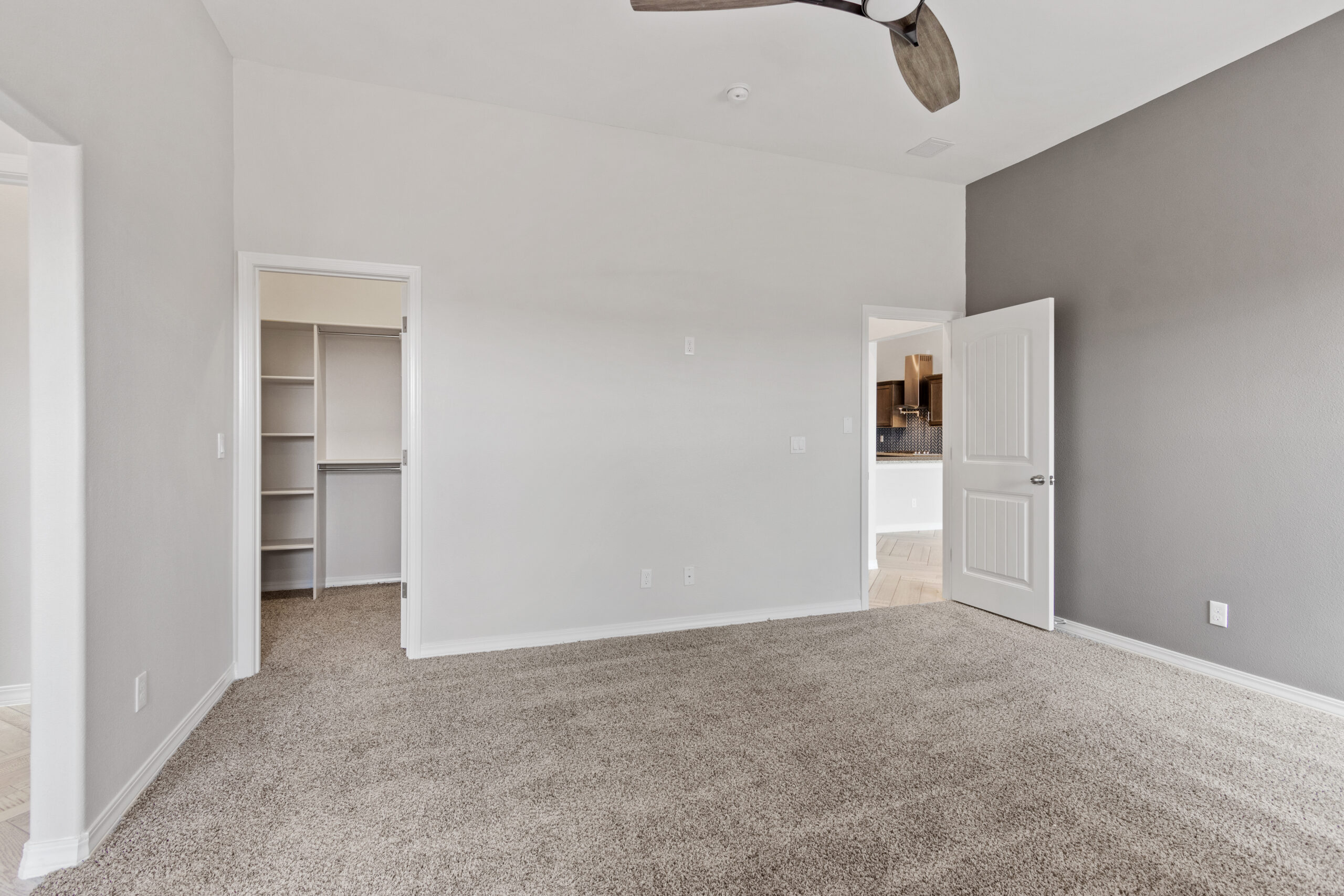 Primary bedroom in The Juniper with neutral carpet, gray accent wall, and walk-in closet access.