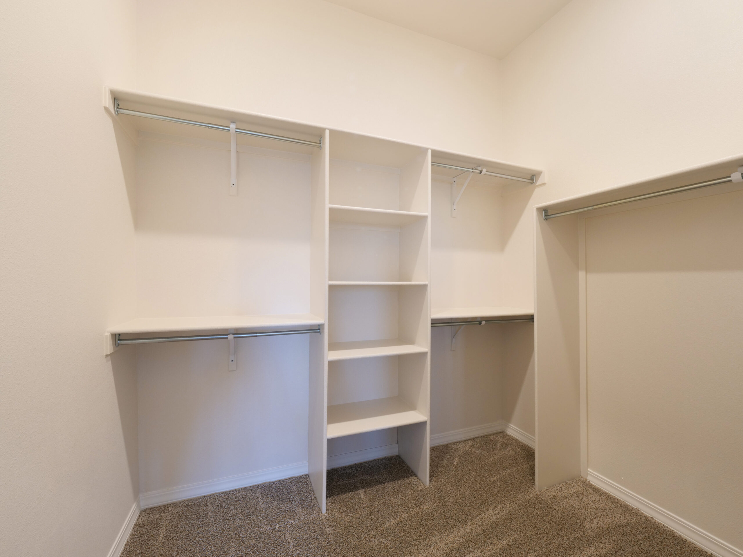 Spacious walk-in closet in The Rose model by Zia Homes with built-in shelves, multiple hanging rods, and neutral carpet flooring.