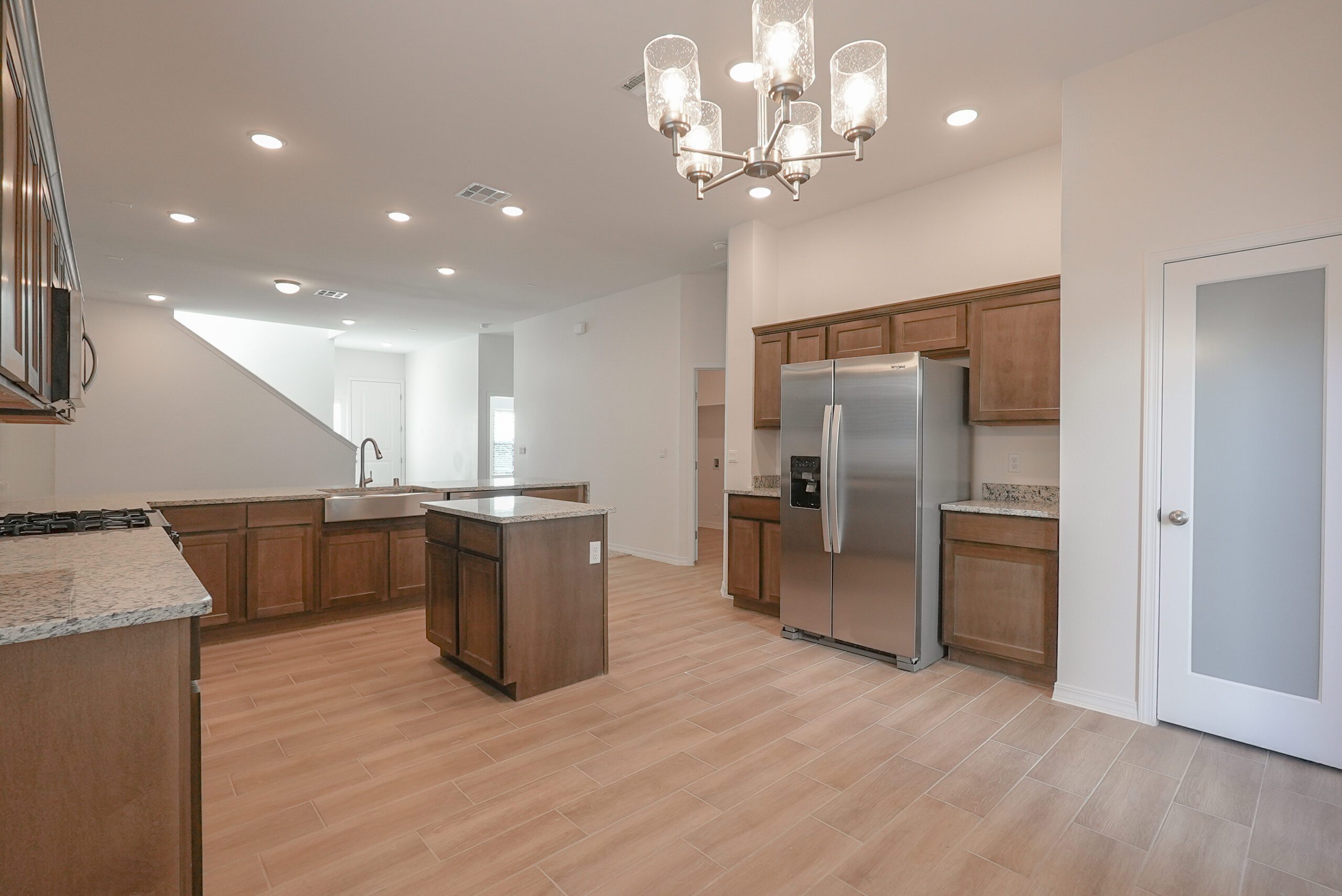 Modern kitchen in The Playa home by Zia Homes featuring granite countertops, stainless steel appliances, wood-look tile flooring, and a central island.