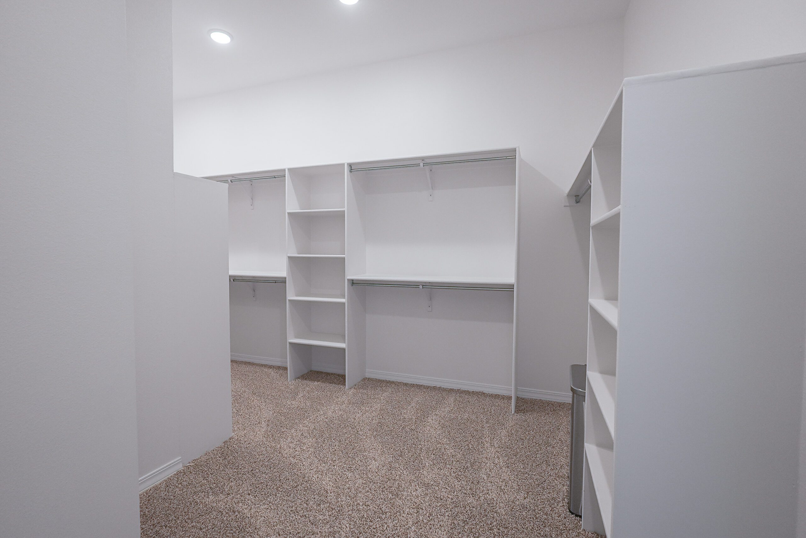 Walk-in closet in The Playa home by Zia Homes featuring built-in white shelving, double hanging rods, and soft carpet flooring.