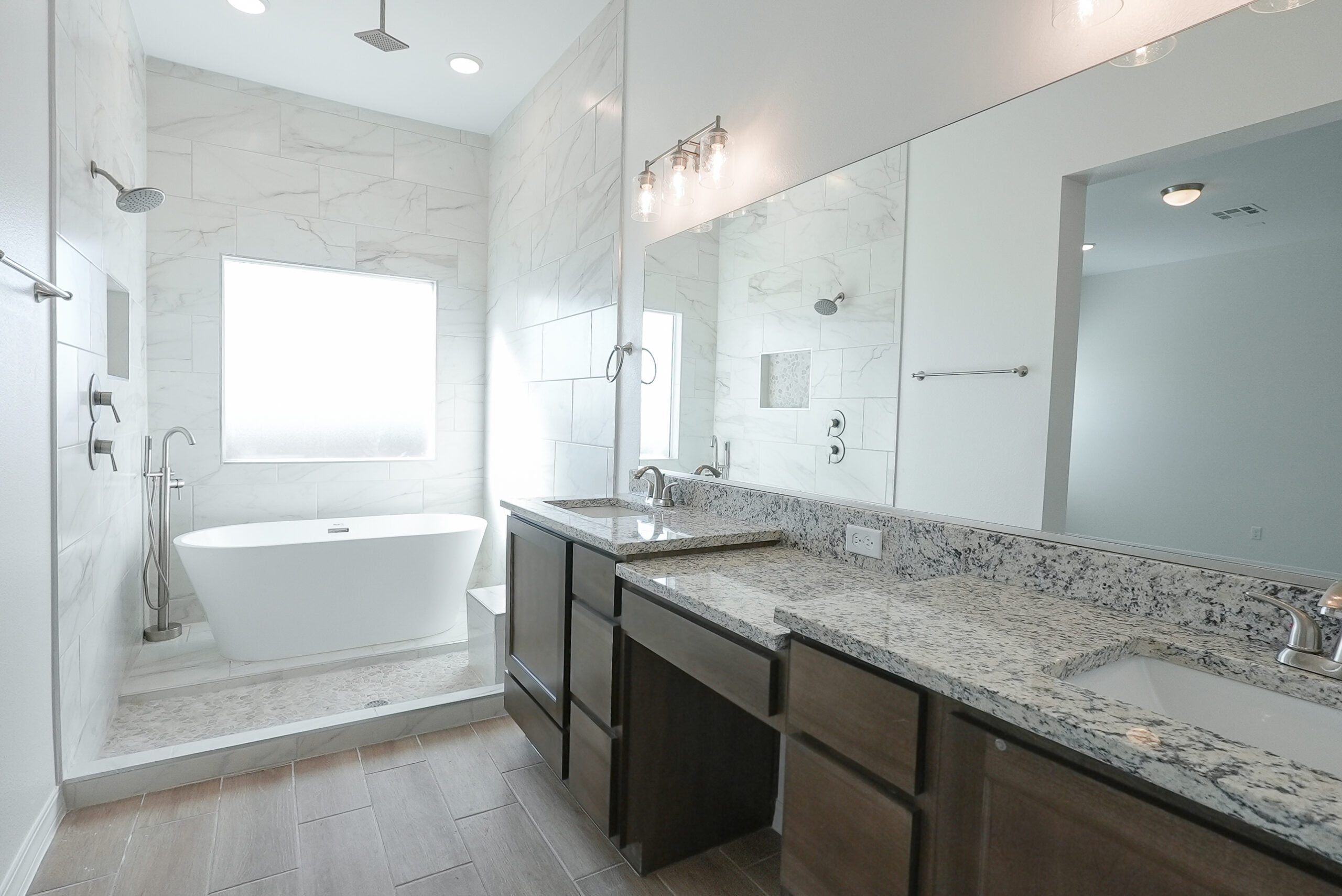Luxury master bathroom in The Playa model by Zia Homes featuring a freestanding soaking tub, walk-in shower with rainfall showerhead, and dual granite vanities.