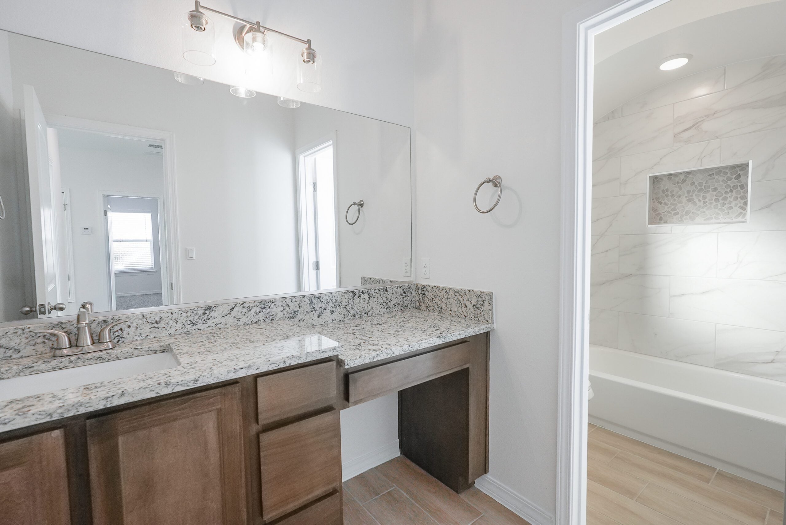 Modern bathroom in The Playa home model by Zia Homes featuring granite countertop vanity and tiled shower with inset niche.