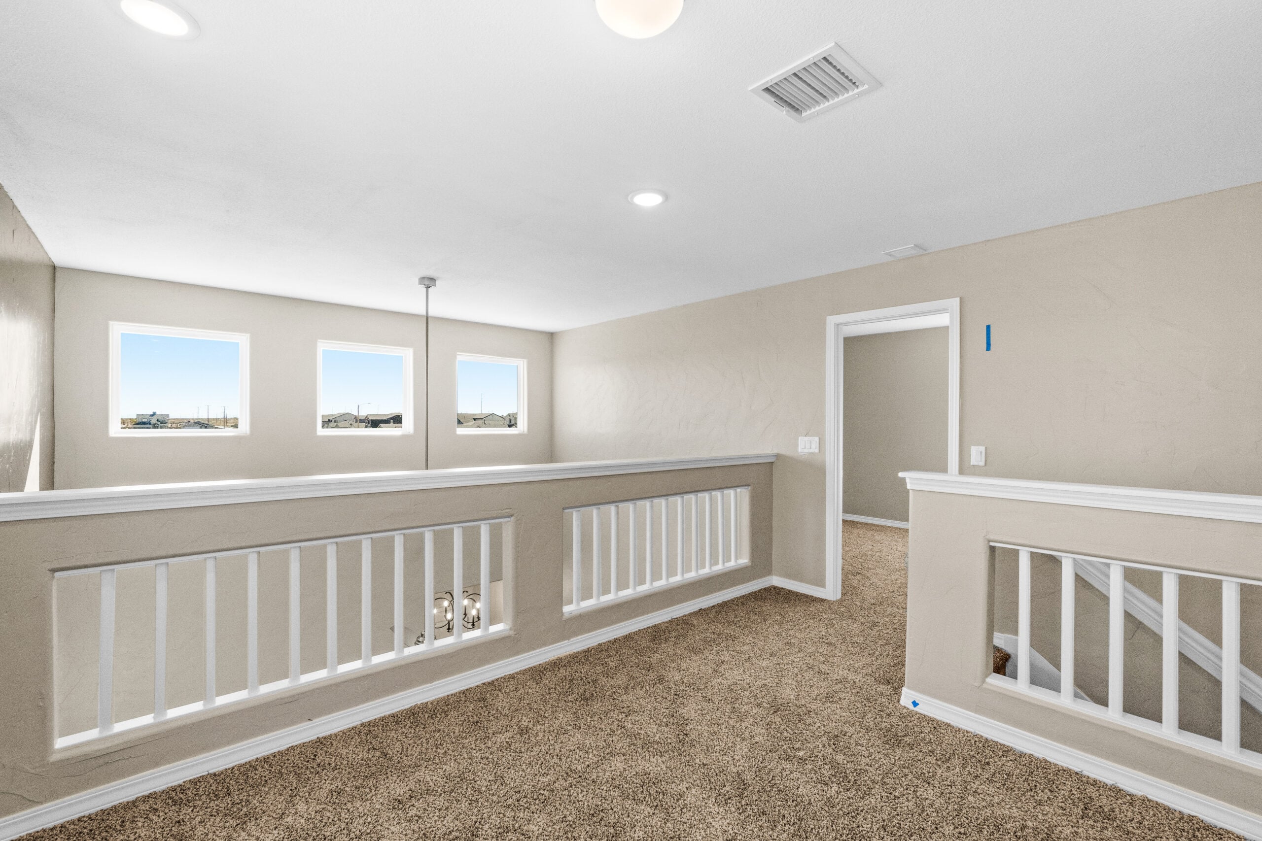 Upstairs loft area with carpet flooring and railing in The Trellis floorplan by Zia Homes.