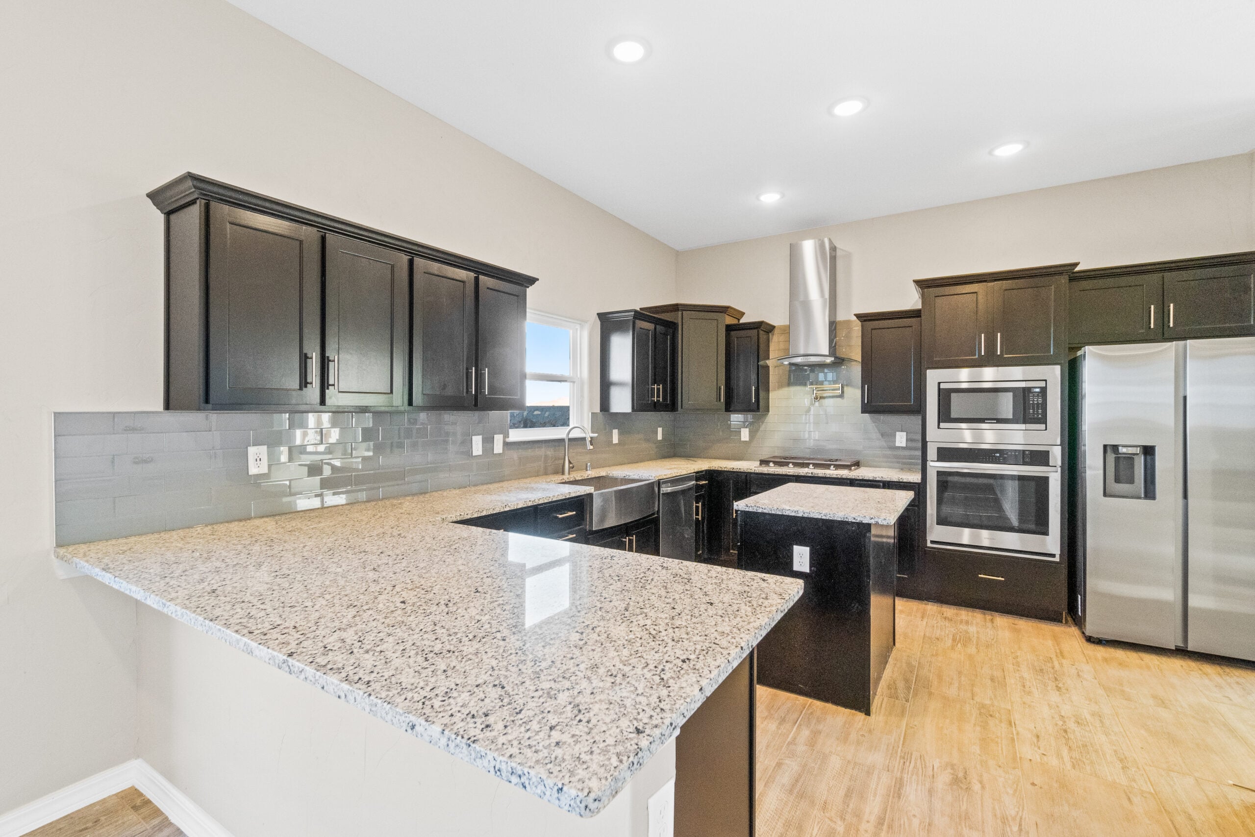 Modern kitchen in The Trellis model featuring granite countertops, stainless steel appliances, and dark wood cabinetry.