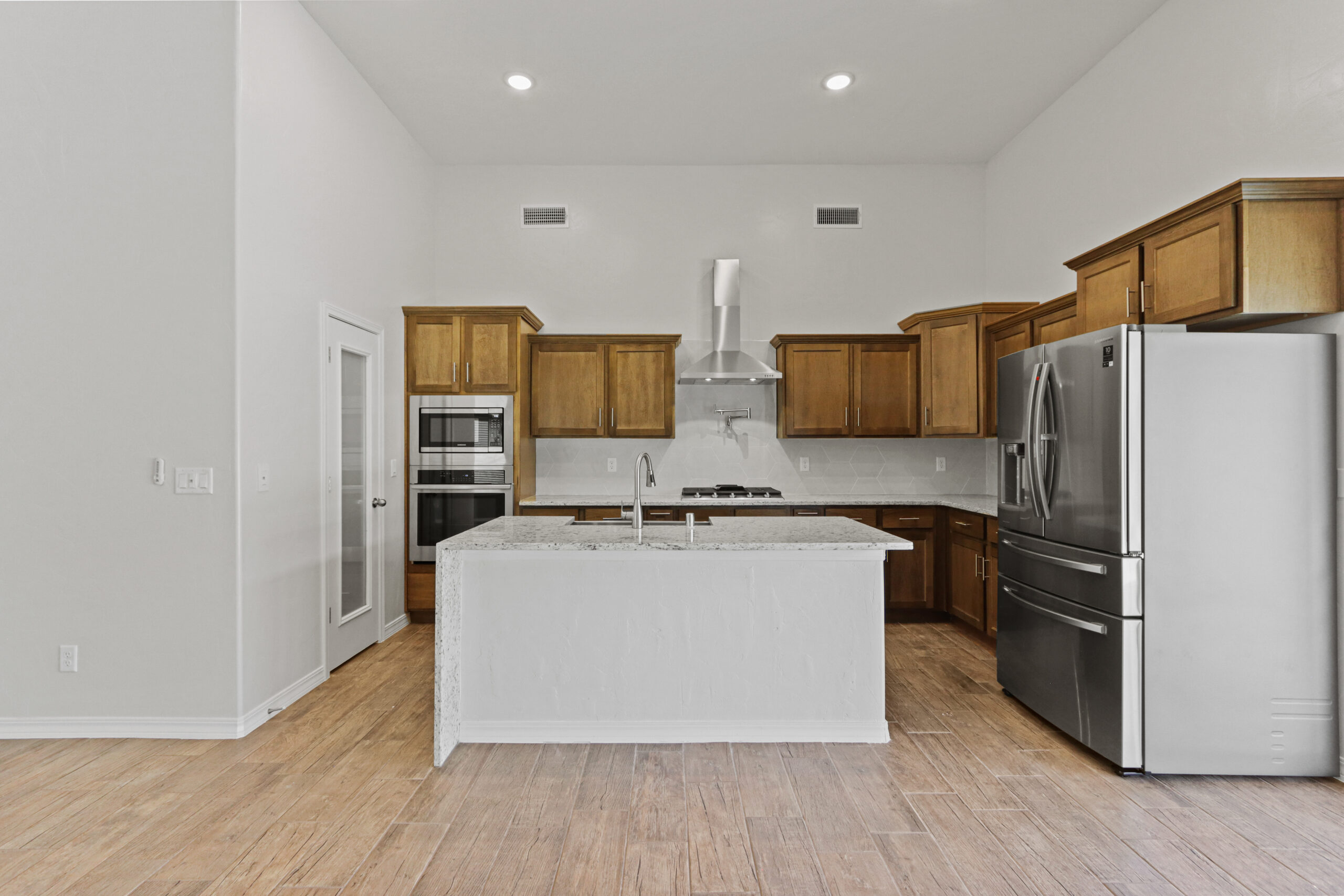 Modern kitchen in The Organza model with wood cabinetry, stainless steel appliances, and a large granite island.