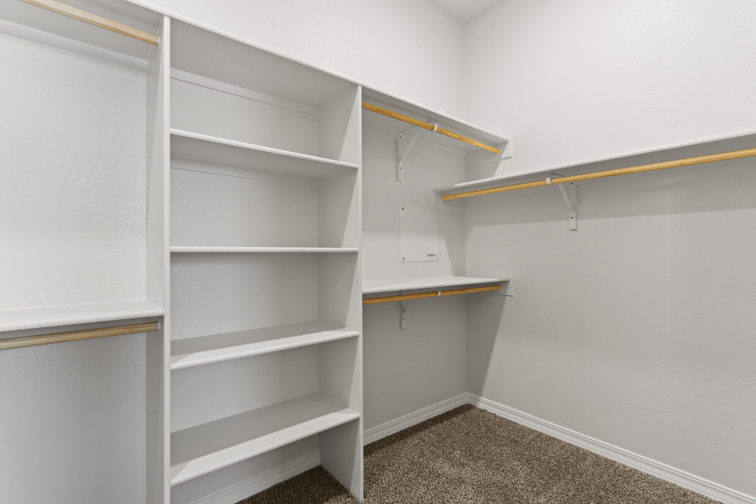 Spacious walk-in closet in The Organza by Zia Homes with built-in shelves, hanging rods, and carpet flooring.