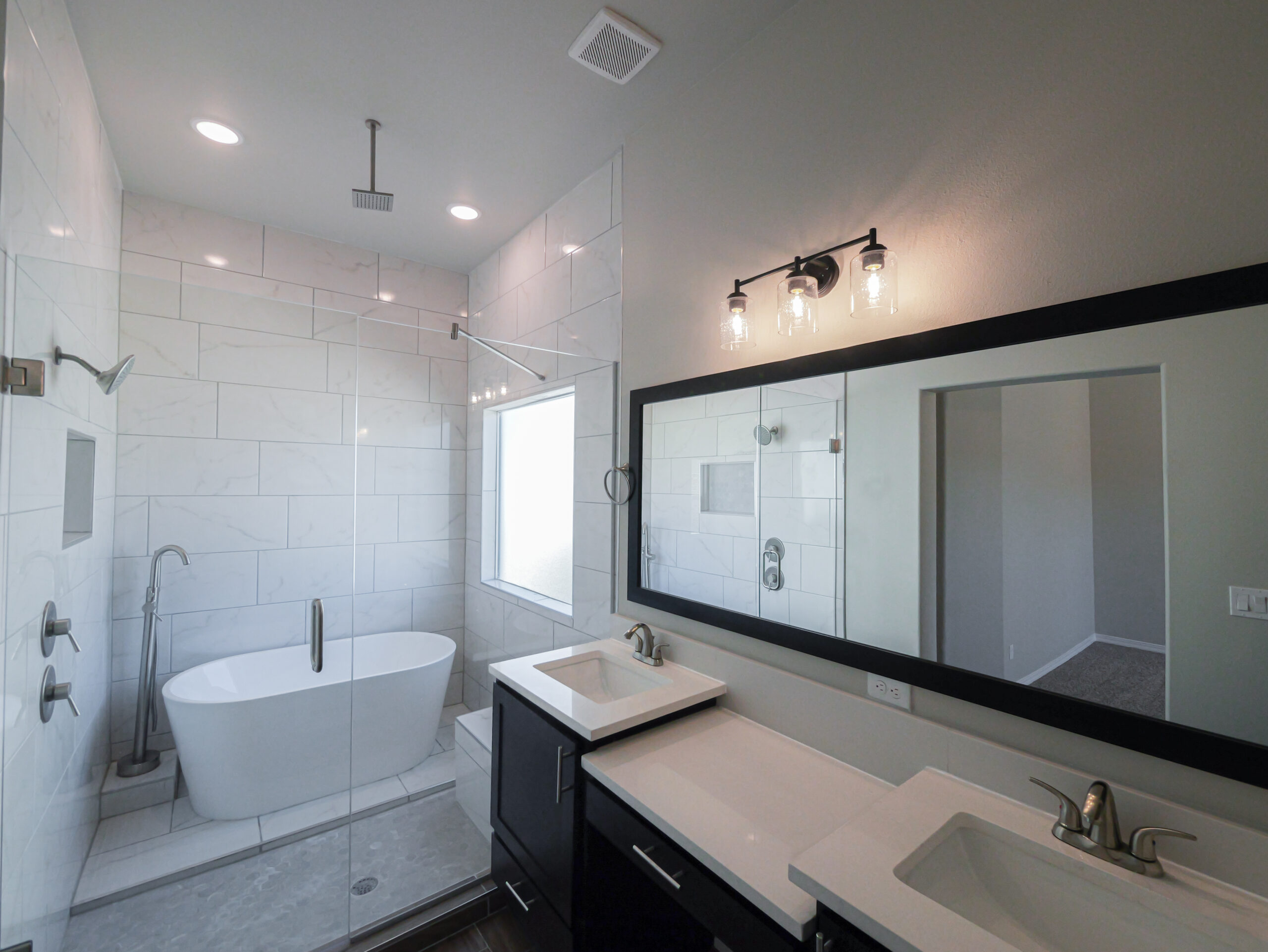 The Arum Bathroom with large mirror, two sinks, and granite countertops. There is a walk-in shower with a free standing tub.