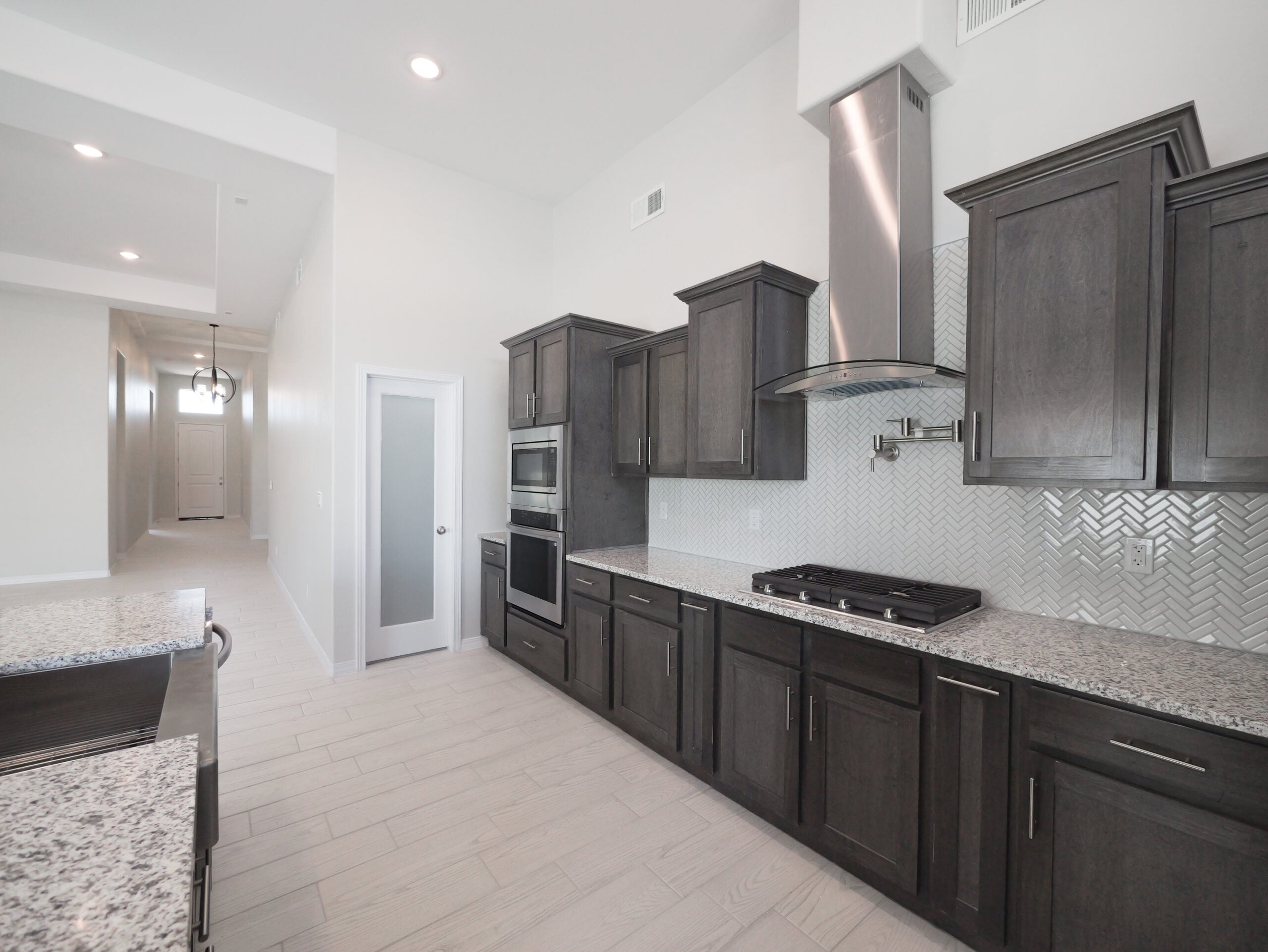 Hibiscus Kitchen with stainless steel appliances, dark wood cabinets, and granite countertops. There is a stacked oven and a oven hood with a pot filler above the stove.