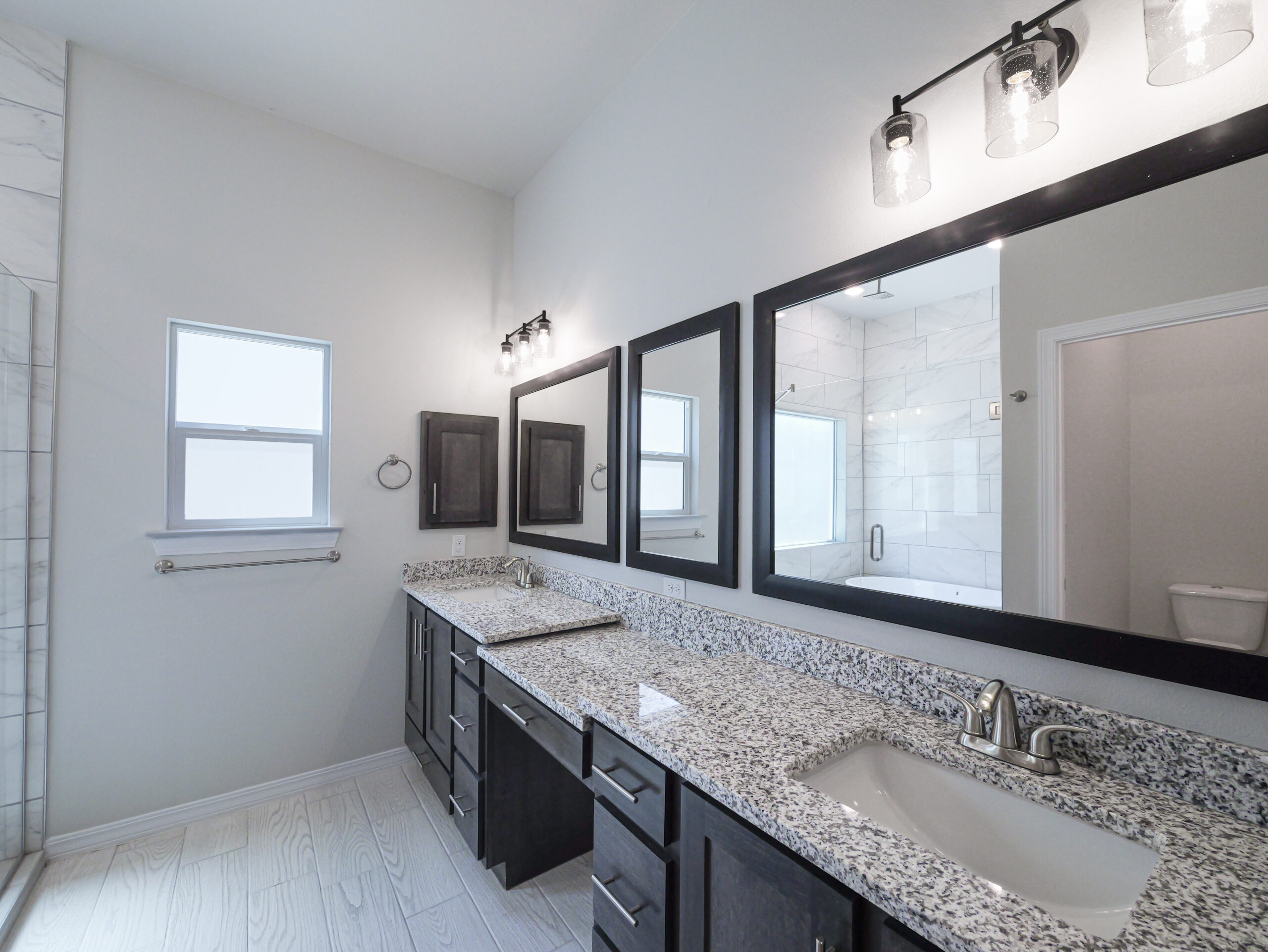 Hibiscus Master Bathroom with two large mirrors and a space for a vanity. Granite countertops and two sinks. Dark wood cabinets.