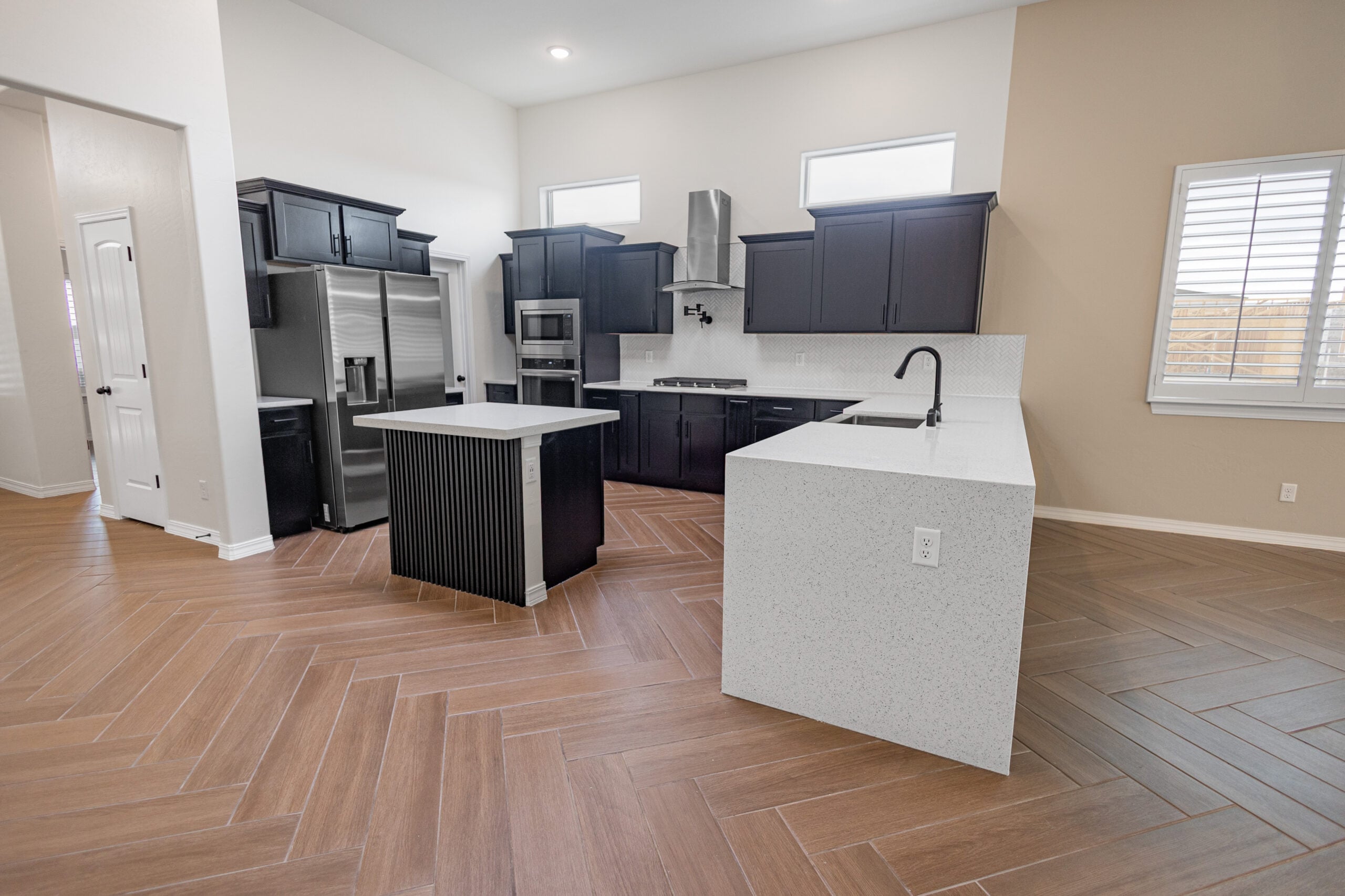 The Daisy Kitchen with dark wood, black and stainless steel appliances, granite countertops, and two windows that sit above the cabinets that allow in natural lighting.